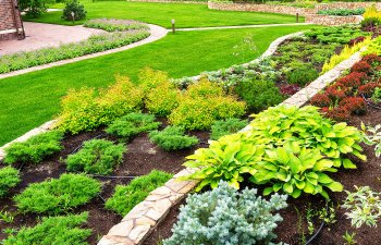 A well-maintained garden with various shrubs and plants bordered by stone pathways and manicured lawns.